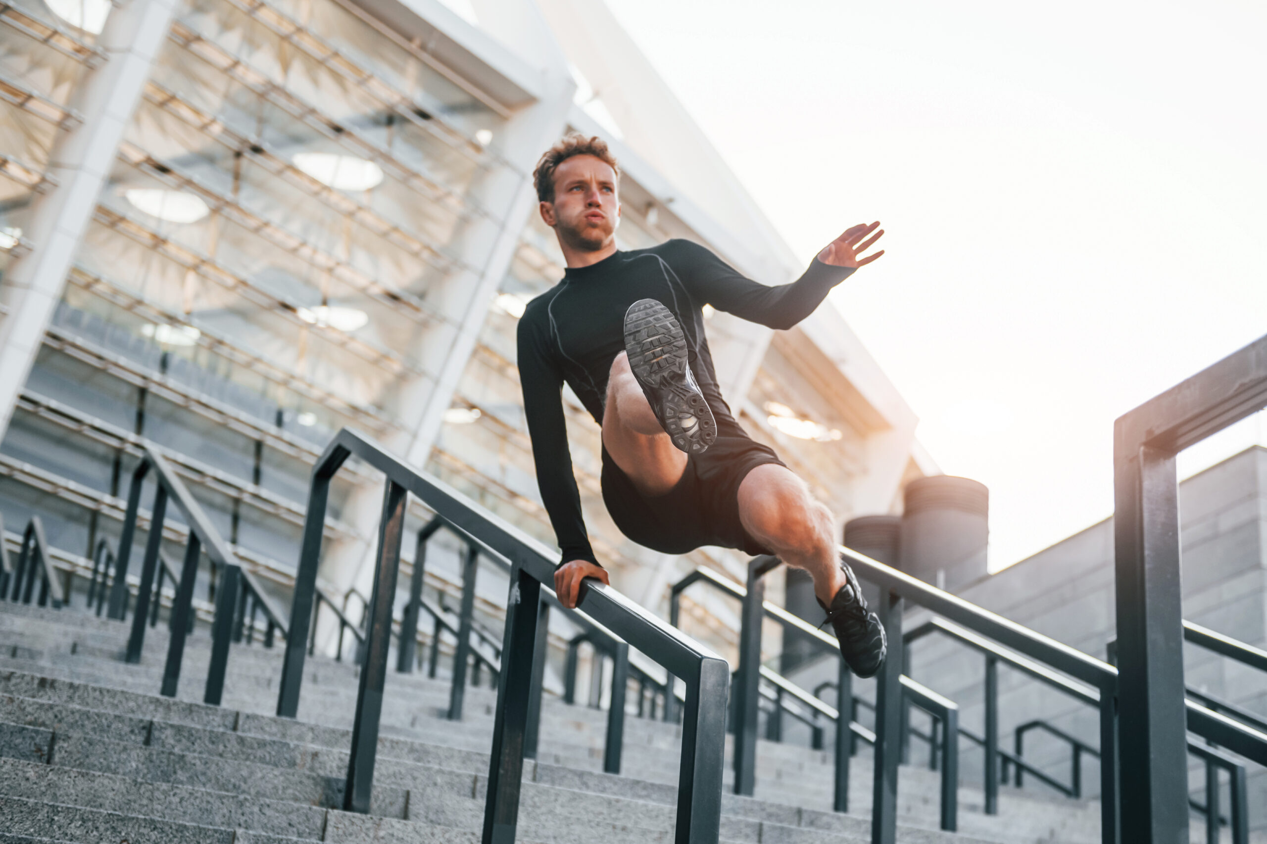 Does parkour. Young man in sportive clothes have workout outdoors at daytime.