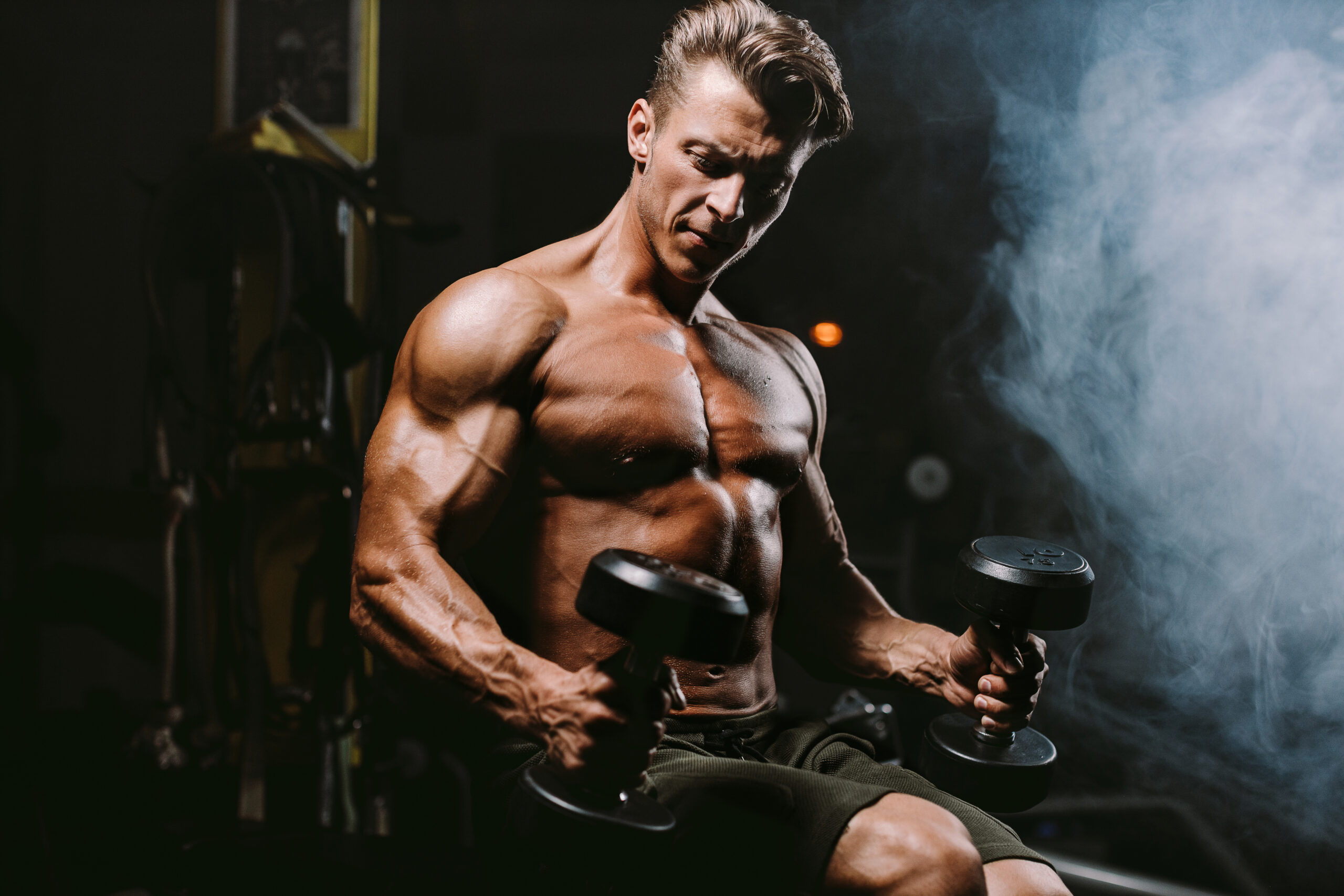 Attractive muscular bodybuilder with dumbbells in gym.