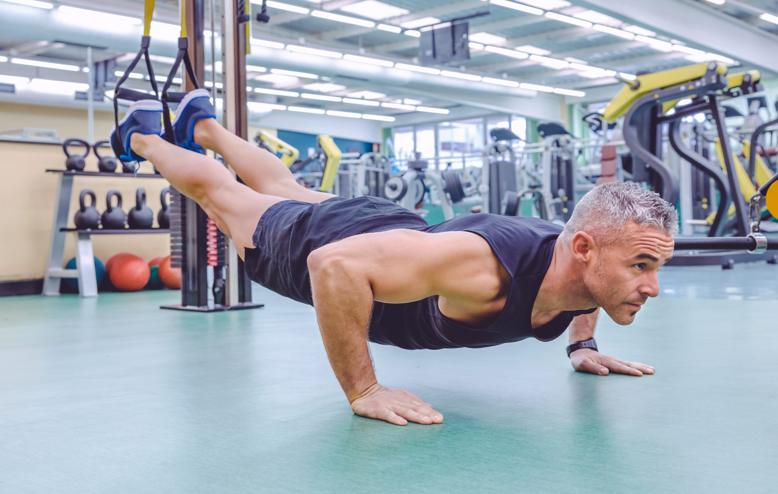 Handsome man doing hard suspension training with fitness straps in a fitness center. Healthy and sporty lifestyle concept.